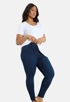 Camicia a maniche corte grigio chiaro abbinata a jeans attillati blu scuro. La camicia ha un collo rotondo e una vestibilità comoda.