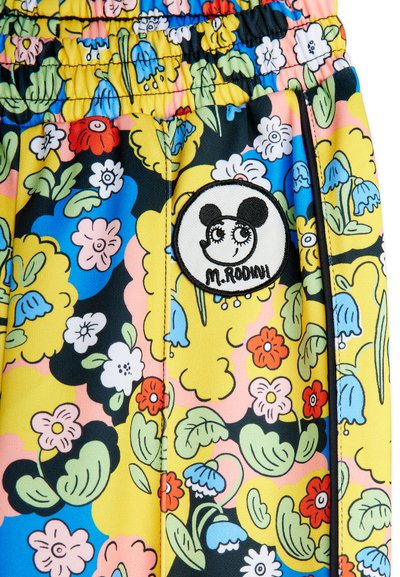 Tejido floral de colores con una cintura elástica y un parche circular que presenta un rostro estilizado y el texto "M. Rodini".