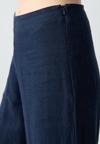 Navyblauwe linnen broek met een gladde textuur, hoge taille en discrete zijrits. Heeft een wijde pijp en een eenvoudige uitstraling.