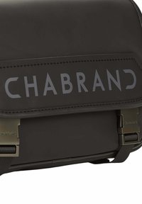 Bolso bandolera negro con acabado mate, con logo "CHABRAND" en relieve, correa ajustable y acentos metálicos. Diseño funcional y compacto.