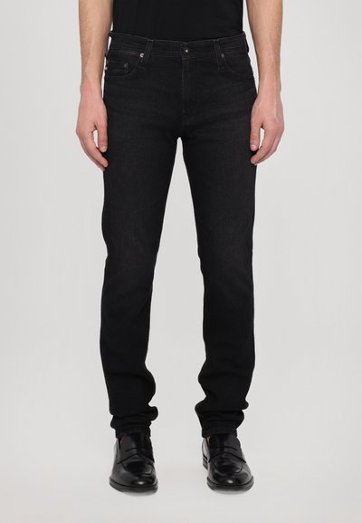 Zwarte denim jeans met een slim fit, voorzien van een middelhoge taille, vijf zakken en subtiele stiksels. Gecombineerd met zwarte nette schoenen.