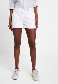 Vita denimshorts med uppvikt fåll, framsidans fickor, metalldetaljer och broderad text på midjebandet. Matchas med ljusgrå sneakers.