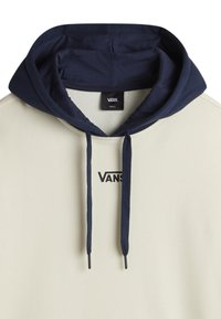 Beige hoodie with a navy blue hood, featuring a logo in black and drawstrings. Soft texture with a regular fit and simple design.