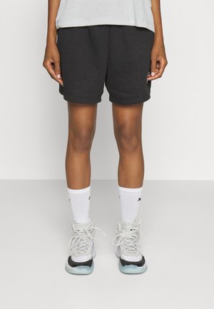 Μαύρο βαμβακερό σορτς με χαλαρή εφαρμογή, διακριτές λεπτομέρειες ραφής, συνδυασμένα με λευκές κάλτσες μέχρι τον αστραγάλο και γκρίζα αθλητικά παπούτσια με μαύρες λεπτομέρειες.