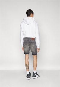 Felpa bianca con cappuccio e lacci, pantaloni corti di jeans grigi con risvolti e scarpe da ginnastica alte nere. Tatuaggio notevole sulla gamba destra.
