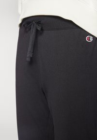 Pantalones de chándal negros con cintura ajustable y un pequeño logo bordado. Textura suave y diseño ajustado. Material de algodón de alta calidad.