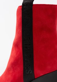 Botín de tobillo de ante rojo con tirador de tela negra que presenta el logotipo grabado "Calvin Klein Jeans".