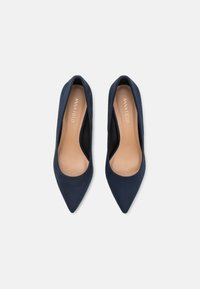 Mörkblå mocka pumps med spetsig tå och slät yta. Inuti finns en beige innersula med "ANNA FIELD"-logotyp.