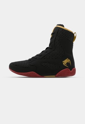 Baskets montantes en mesh noir et matériau synthétique, avec des accents texturés, une semelle en caoutchouc rouge et des détails dorés sur la cheville.