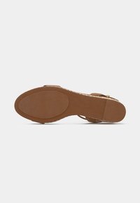 Brown sandal sole with textured oval grip areas at the toe and heel, and a thin strap with a small buckle.