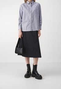 Camicia a righe blu con taschino sul petto, gonna midi nera, borsa a tracolla nera e stivaletti neri con suola spessa.