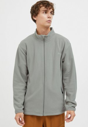 Fleecejacke in Hellgrau mit hohem Kragen, Frontreißverschluss und Seitentaschen. Verfügt über eine strukturierte Oberfläche und dezente Logodetails.