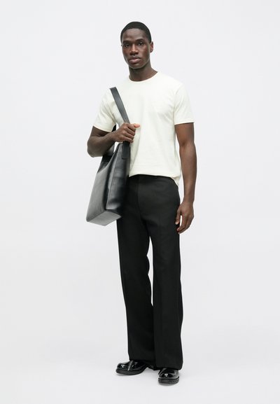 Camiseta de manga corta color crema, pantalones negros de pierna ancha y bolso de hombro de cuero negro. Texturas suaves y diseño minimalista en todo el conjunto.