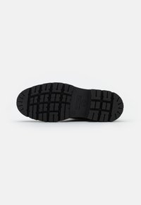 Suela de zapato de goma negra con un patrón de relieve texturizado, que presenta profundos surcos para tracción y detalles de marca en relieve.