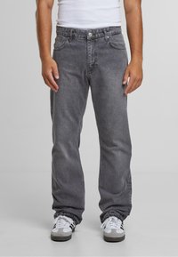 Jean en denim gris à coupe décontractée, avec cinq poches et un délavage subtil. Associé à des baskets blanches avec des accents gris.