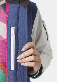 Kleurijke jas met een blauwe denim body, een roze voering, een witte rits en gebreide groene kraagmanchetten. Gelaagd ontwerp met textuur.