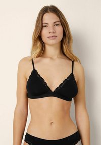 Bralette nera con pizzo, tessuto morbido, coppe triangolari, spalline regolabili e design senza cuciture. Abbinato a slip neri coordinati.