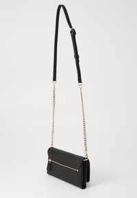 Sac bandoulière noir avec une finition texturée, une bandoulière en chaîne métallique dorée, une poche zippée et un fermoir à rabat. Design compact et rectangulaire.