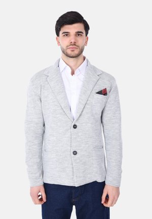 Cardigan grigio lavorato a maglia con maniche lunghe, colletto a scialle, due tasche frontali e un fazzoletto nero con un motivo rosso.
