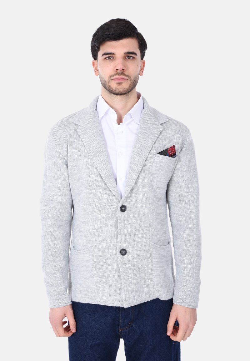 Cardigan grigio lavorato a maglia con maniche lunghe, colletto a scialle, due tasche frontali e un fazzoletto nero con un motivo rosso.