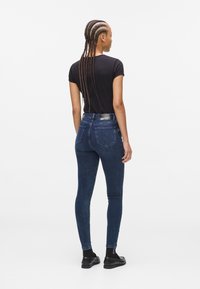Blugi skinny din denim albastru închis, cu un fit elastic, având două buzunare la spate și o etichetă pe talie. Bluză neagră cu mânecă scurtă.