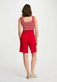Pantaloni corti rossi a vita alta abbinati a una canotta senza maniche a righe rosse e bianche. Il tessuto appare liscio, con una silhouette aderente.
