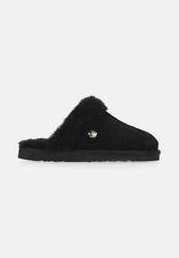 Sorte slippers lavet af ruskind med en fluffy indvendig kant, flad gummisål og et lille dekorativt sølvemblem på siden.