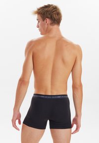 Schwarze Boxershorts mit einem weichen elastischen Bund, der das Label "JBS UNDERWEAR" trägt, dargestellt an einem männlichen Modell aus der Rückansicht.