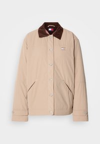 Veste beige à boutons avec col en velours côtelé marron foncé, deux poches avant inclinées et un petit logo sur la poitrine.