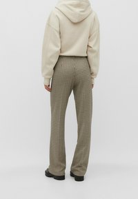 Cappotto corto crema abbinato a pantaloni con motivo pied de poule. I pantaloni presentano una vita alta e una gamba dritta, con tessuto testurizzato.