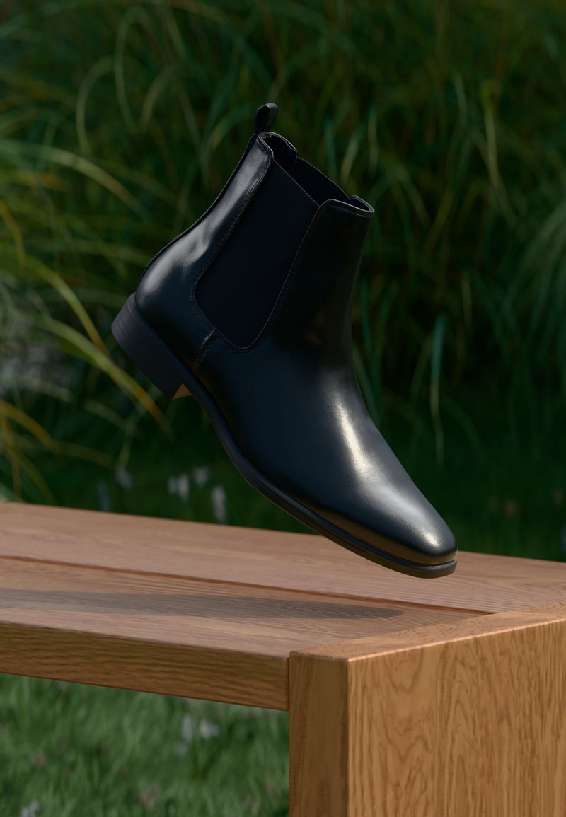 Schwarze Leder-Chelsea-Boots, die über einer Holzbank schweben, mit Gras und Pflanzen im Hintergrund.