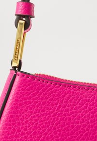 Pink leather handbag featuring a smooth texture, gold hardware, and a zipper detail at the top, with contrasting black edges.