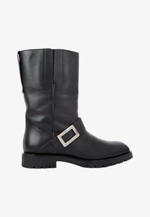 Botte en cuir noire mi-mollet avec une bride à boucle carrée argentée et une semelle épaisse crantée.