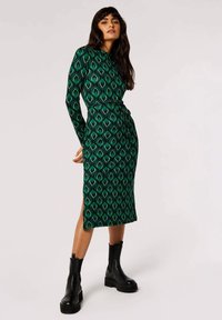 Abito midi verde a fantasia con design a portafoglio, maniche lunghe, uno spacco laterale e abbinato a stivali alla caviglia neri e chunky.