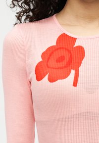 Ριμπ ροζ τοπ με μεγάλο κόκκινο λουλουδάτο σχέδιο. Εφαρμοστό σχέδιο με στρογγυλή λαιμόκοψη και μακριά μανίκια. Ομαλή υφή χωρίς ιδιαίτερες λεπτομέρειες.