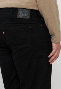 Sorte Levi's 541 jeans med teksturert stoff, en rektangulær baklapp og to baklommer med detaljer i rødt.