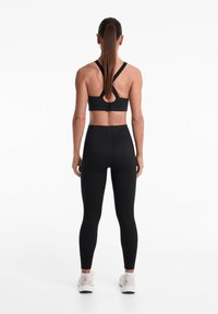 Top sportiv negru, cu bretele încrucișate, asortat cu colanți negri cu talie înaltă. Textură netedă, design minimalist și formă ajustată.