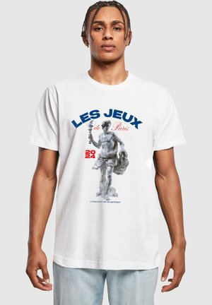 Valge puuvillane T-särk, millel on graafika kujust, mis hoiab torch'i, sinise tekstiga "LES JEUX de Paris 2024" ja tsitaat all.