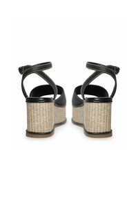 Sandalias de cuña negras con tacón trenzado de fibra natural, correa en el tobillo ajustable y detalles de costura blanca. Parte superior suave y suela plana.