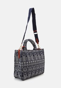 Plátěná kabelka s geometrickým vzorem v námořnické modři a krémové barvě, zdobená červenými koženými detaily a odnímatelným popruhem. Strukturovaný obdélníkový tvar.