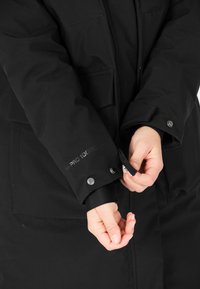 Svart vattentät jacka med en slät yta, utrustad med silverfärgade tryckknappar och justerbara manschetter. "W PRO 10000"-logotypen synlig på ärmen.