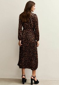 En långärmad klänning med djurmönster i brunt och svart, med en plisserad design och en insvängd midja, kombinerad med svarta klacksandaler.