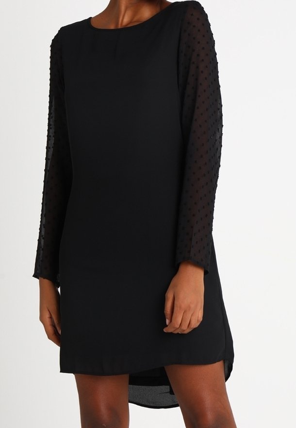 Robe noire avec un corps en tissu uni et des manches longues en tulle à pois transparent, dotée d'un col rond et d'un ourlet légèrement arrondi.