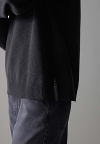 Black knit sweater featuring a ribbed hem and side slits, paired with dark gray jeans, showcasing a soft texture and relaxed fit.