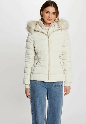 Doudoune blanche avec capuche en fourrure amovible, zip doré, poches latérales et accents de taille élastiqués. Poignets côtelés et design matelassé.
