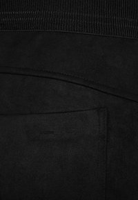 Pantaloni neri con una texture liscia e morbida, dotati di una vita a coste e dettagli delle tasche curve. Nessun marchio o motivo visibile.