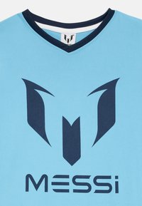 Šviesiai mėlyna marškinėliai su tamsiai mėlynu V formos apykakle. Priekyje yra didelis tamsiai mėlynas logotipas ir tekstas "MESSi". Lygi tekstūra, komandos dizainas.