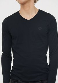 T-shirt noir à manches longues et col en V, fabriqué en coton doux. Doté d'un logo discret sur la poitrine et d'un design ajusté, avec des détails de poignet et d'ourlet standards.