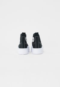 Sorte semskede høje sneakers med hvide gummisåler, der har et cirkulært logopatch og hvide syninger detaljer på bagsiden.