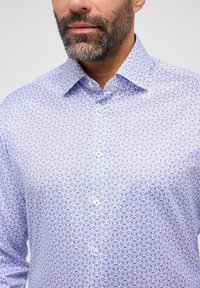 Camicia azzurro chiaro a motivi con piccoli disegni geometrici, colletto a punta e chiusura con bottoni. Realizzata in un tessuto morbido.